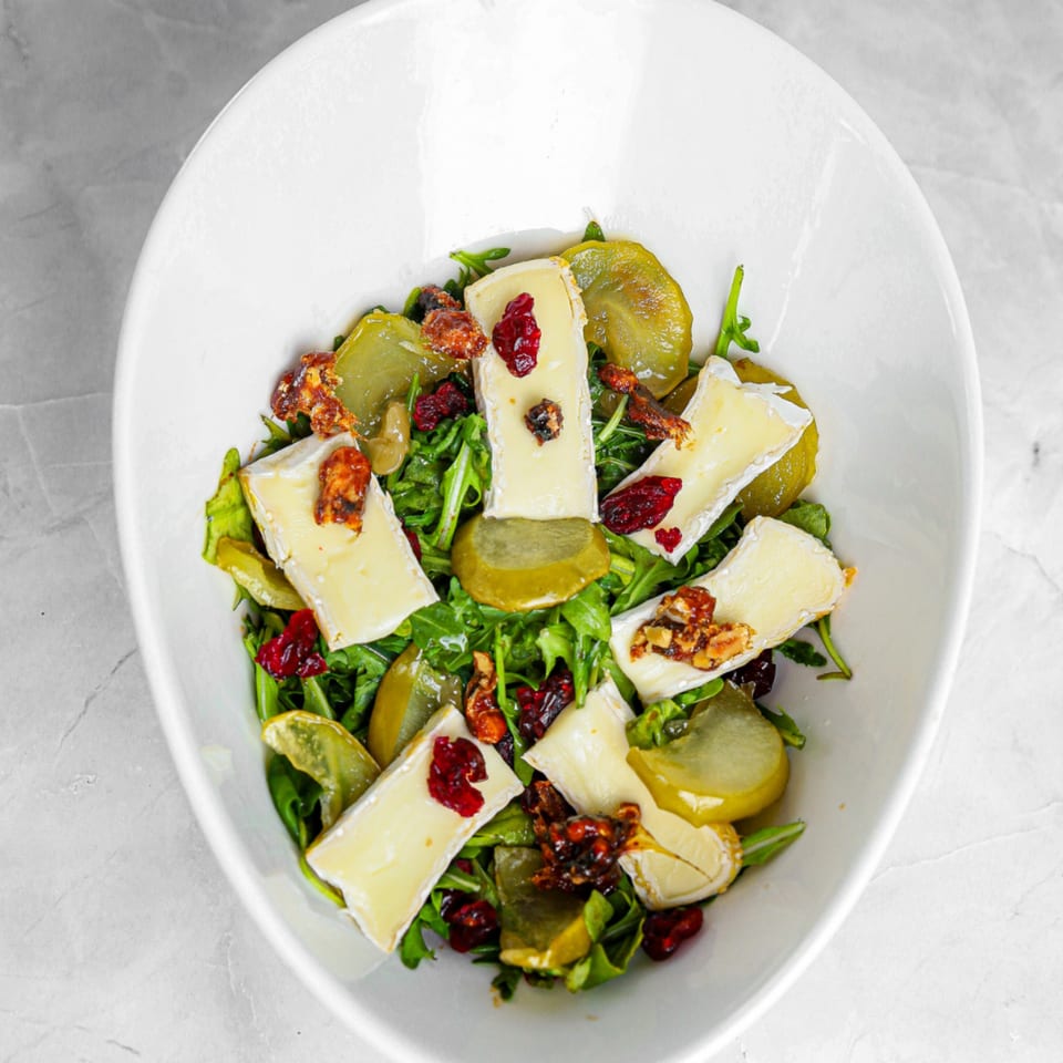 A vibrant Vita Nostra salad with arugula, brie, candied walnuts, dried cranberries, and green apple slices.
