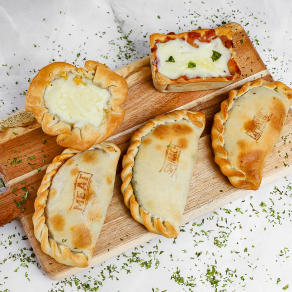 Assortment of Argentinian empanadas and a tart, some labeled "MEAT" and "SPINACH", on a wooden board.